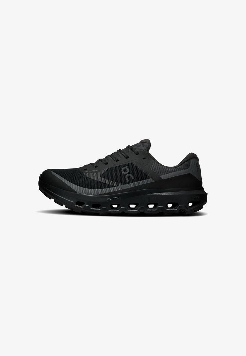 Baskets de sport noires avec dessus en mesh, fermeture lacets, semelle coussinée avec trous de ventilation, et logo de marque sur le côté et le talon.