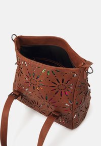 Brązowa torebka skórzana z perforacjami i kwiatowymi wycięciami, zawierająca kolorowe wnętrze. Posiada podwójne uchwyty oraz zamek błyskawiczny na górze.