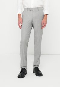 Calças de mesa cinza claro com um acabamento texturizado, frente lisa, passantes para cinto e um corte slim, combinadas com sapatos formais pretos.