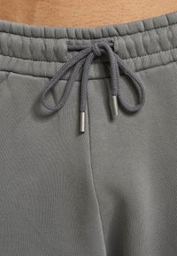 Pantalones joggers de algodón gris con cintura ajustable mediante cordón con textura trenzada y extremos metálicos; tela texturizada con un acabado suave.
