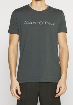 Mand iført en mørkegrå t-shirt med korte ærmer og teksten "Marc O’Polo" centreret på brystet, kombineret med sorte bukser.