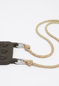 Funda de silicona en marrón oscuro con botones elevados; cuenta con una correa trenzada de múltiples colores con clips de metal y detalle anudado para un acoplamiento seguro.