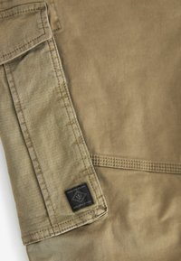 Smeđa tkanina izbliza koja prikazuje teksturiranu površinu i crnu oznaku s natpisom "Premium Grade Durable Goods" u donjem lijevom kutu.