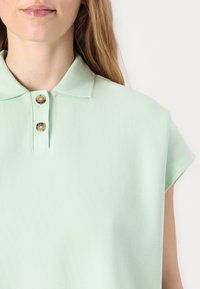 Polo shirt in zachte mintgroene kleur, met een ribbelstructuur, korte mouwen en twee ronde knopen bij de kraag. Schoon en minimalistisch ontwerp.