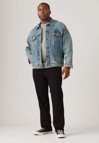 Lichtblauwe spijkerjack over een grijs shirt, gecombineerd met zwarte jeans en zwarte sneakers. De jas heeft een relaxte pasvorm en knoopsluiting.