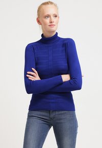 Pullover mit Rollkragen aus kräftigem Blau, mit strukturiertem Paneldesign und geripptem Stoff für eine figurbetonte Passform. Trägt man mit Jeans.