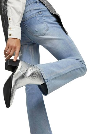 Silberne, metallische Knöchelschuhe mit einem strukturierten Design, kombiniert mit hellblauen, verwaschenen Jeans und einem weißen, knopfbenetzten Hemd.