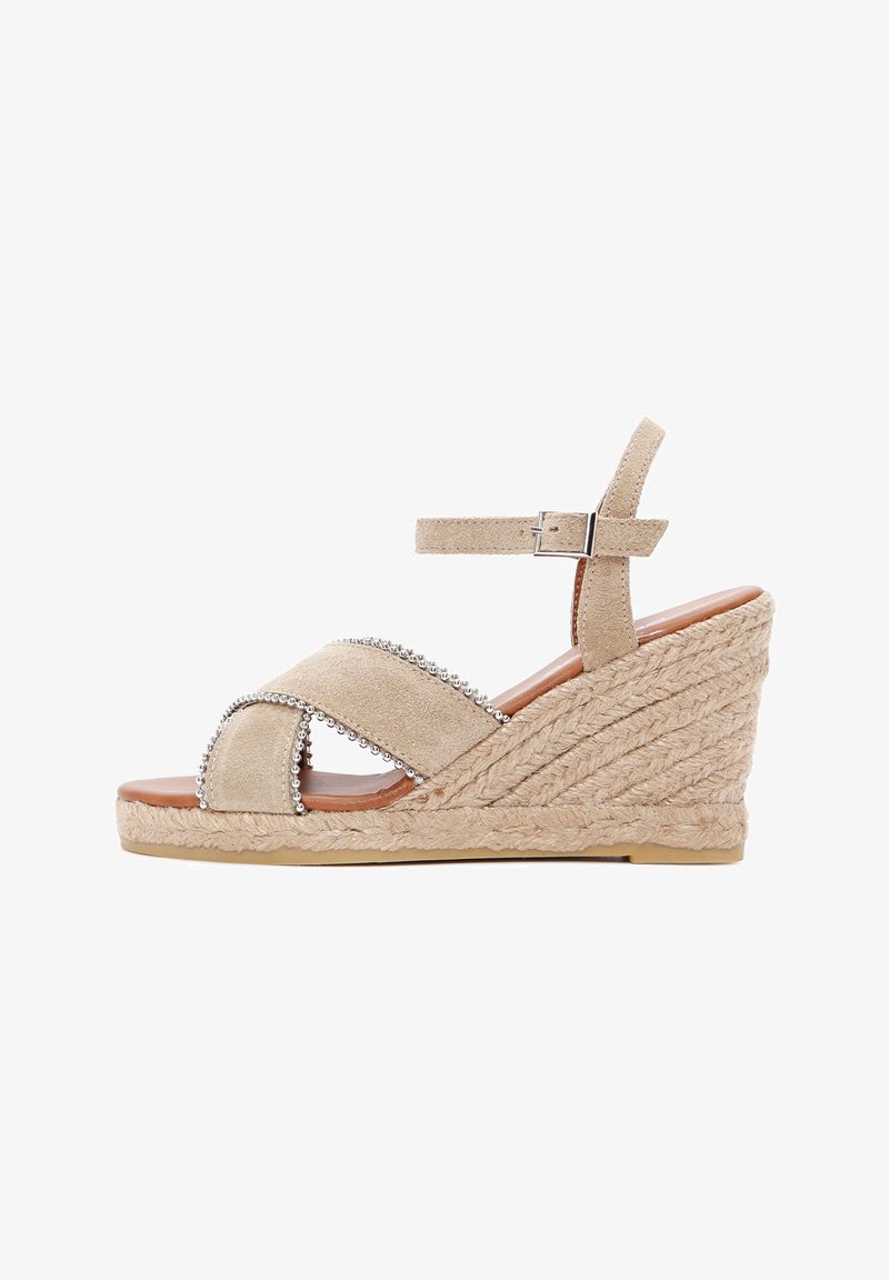 Beige Keilsandale mit einer Jute-Plattform, Wildlederriemen, Kreuzdesign und metallischen Perlenakzenten an den Riemen. Schnallenverschluss am Knöchel.