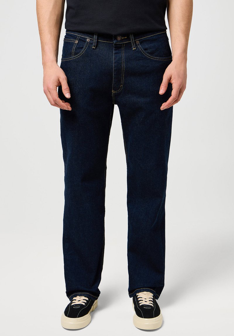 Ciemnoniebieskie dżinsy jeansowe o prostym kroju nogawki, z kontrastującym żółtym przeszyciem, klasycznym wzorem z pięcioma kieszeniami oraz zapinane na guzik.