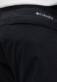 Голям план на черна тъкан с марка Columbia с зашит хоризонтален джоб на горната част на гърба на дреха.