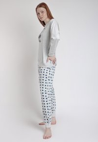 Camiseta de manga larga gris claro con un estampado gráfico, combinada con pantalones de pijama gris claro con un patrón de corazones azules. Ajuste suave, diseño casual.