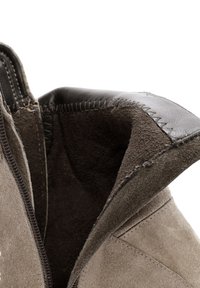 Bottines en daim gris avec une doublure intérieure douce, des accents en cuir et des surpiqûres contrastantes le long des bords. Détail de fermeture éclair visible.