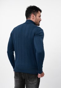 Marineblauw trui met verticale ribbeltextuur, hoge kraag en slim fit ontwerp. Meerkleurige gebreide stof met een strakke tailleband.