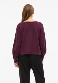 Paarse top met lange mouwen, een losse pasvorm en een brede halslijn. Gladde textuur met opgeblazen mouwen, gecombineerd met een zwarte broek.