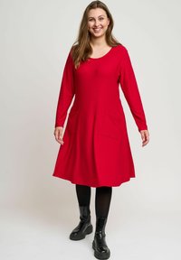 Röd klänning med långa ärmar, rundad halsringning och två framfickor. Tillverkad av textil med struktur, kombinerad med svarta ankelstövlar.