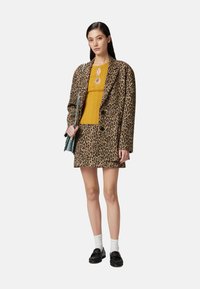 Combinazione di blazer in stampa leopardata e mini gonna in un tessuto morbido, abbinata a una maglietta gialla a coste. Gli accessori includono una piccola borsa.