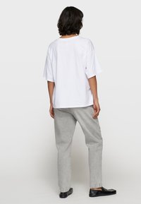 Camiseta blanca de gran tamaño con mangas cortas, combinada con pantalones rectos de color gris claro. Unos zapatos planos negros completan el conjunto.
