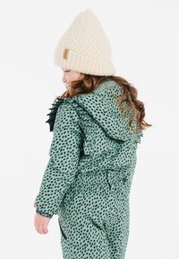 Groen patroon buitenkleding met gerimpelde mouwen, elastische tailleband en zwarte accenten. Gecombineerd met een crèmekleurige gebreide beanie.