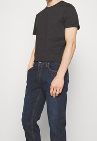 Czarna bawełniana koszulka z krótkim rękawem w połączeniu z ciemnymi dżinsami. Koszulka ma okrągły dekolt i luźny krój. Dżinsy mają klasyczny, pięciopocketowy design.