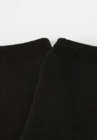 Sorte bomuldsstrømper med ribbede manchetter, der har en glat overflade og sømløst design, set fra en tæt vinkel.