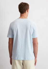 Hellblaues Kurzarm-T-Shirt aus weicher Baumwolle, mit Rundhalsausschnitt und lockerer Passform, samt glatter Textur und minimaler Ausstattung.