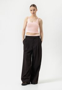 Débardeur ajusté rose, pantalon large à rayures noires avec poches, et chaussures robustes noires. Design simple et couleurs contrastées.