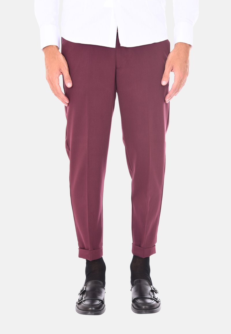 Pantaloni su misura bordeaux con una vestibilità slim, caratterizzati da orli arrotolati e un tessuto morbido. Indossati con scarpe nere con fibbia e calze scure.