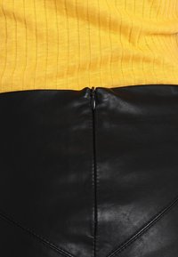 Gul ribbad stickad topp möter en slät svart läderkjol med en central dragkedja och vinklad sömdekoration bak.