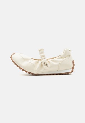 Chaussure plate décontractée pour femme de couleur crème avec bride élastique et semelle marron texturée, vue de profil sur fond uni.