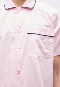Ροζ κοντομάνικο πουκάμισο με κουμπιά εμπρός, τσέπη στο στήθος με περίγραμμα σε σκούρο χρώμα και γιακά με σκουρόχρωμη επένδυση.