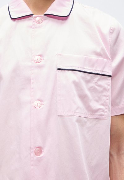 Ροζ κοντομάνικο πουκάμισο με κουμπιά εμπρός, τσέπη στο στήθος με περίγραμμα σε σκούρο χρώμα και γιακά με σκουρόχρωμη επένδυση.