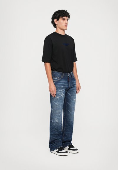Tricou negru din bumbac cu mâneci scurte, asortat cu blugi denim blue destrămați, cu o croială lejeră și petice. O pereche de tenisi alb-negru completează ținuta.