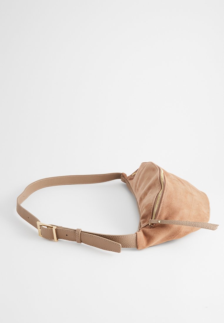 Sac banane en suède beige avec une poche zippée à l'avant, de forme plate, sangle ajustable et texture lisse, idéal pour un usage mains libres.