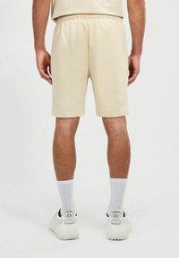 Pantalones cortos deportivos beiges con una cintura elástica, textura de tela suave, hasta la rodilla, combinados con calcetines blancos y zapatillas deportivas.