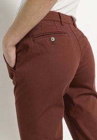 Bordó kalhoty s úzkým střihem, vyrobené z bavlněné směsové tkaniny. Disponují zadní kapsou s knoflíkovým uzávěrem. Hladká textura.