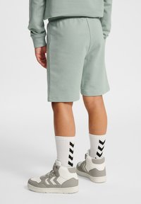 Gröna bomullsshorts med resår i midjan, kombinerade med vita strumpor med svarta chevronmönster och grå högklackade sneakers.