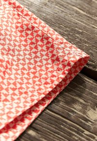 Korall szövet fehér geometriai mintával, amely szívformákat ábrázol. Simább textúra, hajtott szegéllyel, fa felületen elhelyezve.