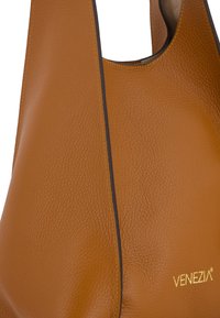 Helle Ledertasche mit strukturierter Oberfläche, akzentuiert durch schwarze Paspeln und gelbe Nähte. Mit einem goldenen Logo-Abdruck.