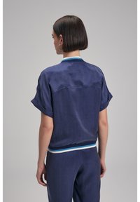 Marinblå kortärmad topp med mjuk textur, med en kontrasterande randig kant vid halsringningen och nederkant. Skräddarsydd design med en avslappnad passform.