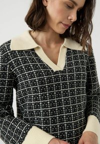 Svartvitt mönstrad tröja med en krämfärgad, ribbad krage och manschetter. Har en v-ringning och textil med struktur.