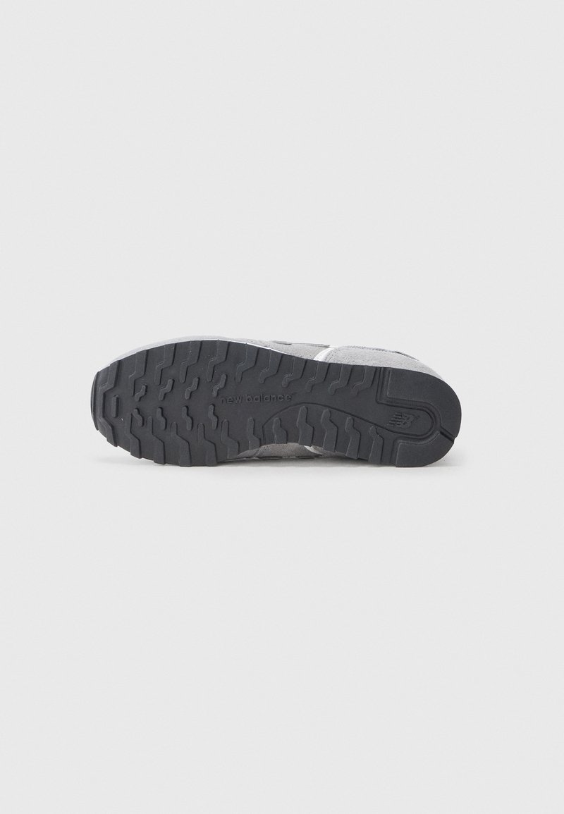 Semelle de sneaker grise avec caoutchouc texturé pour une traction, présentant un logo subtil et un mélange de matériaux lisses et en daim.