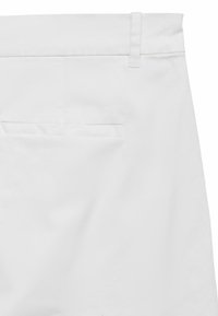 Primer plano de la sección superior trasera de unos pantalones blancos que muestra una trabilla para el cinturón y un bolsillo trasero de ojal sencillo.