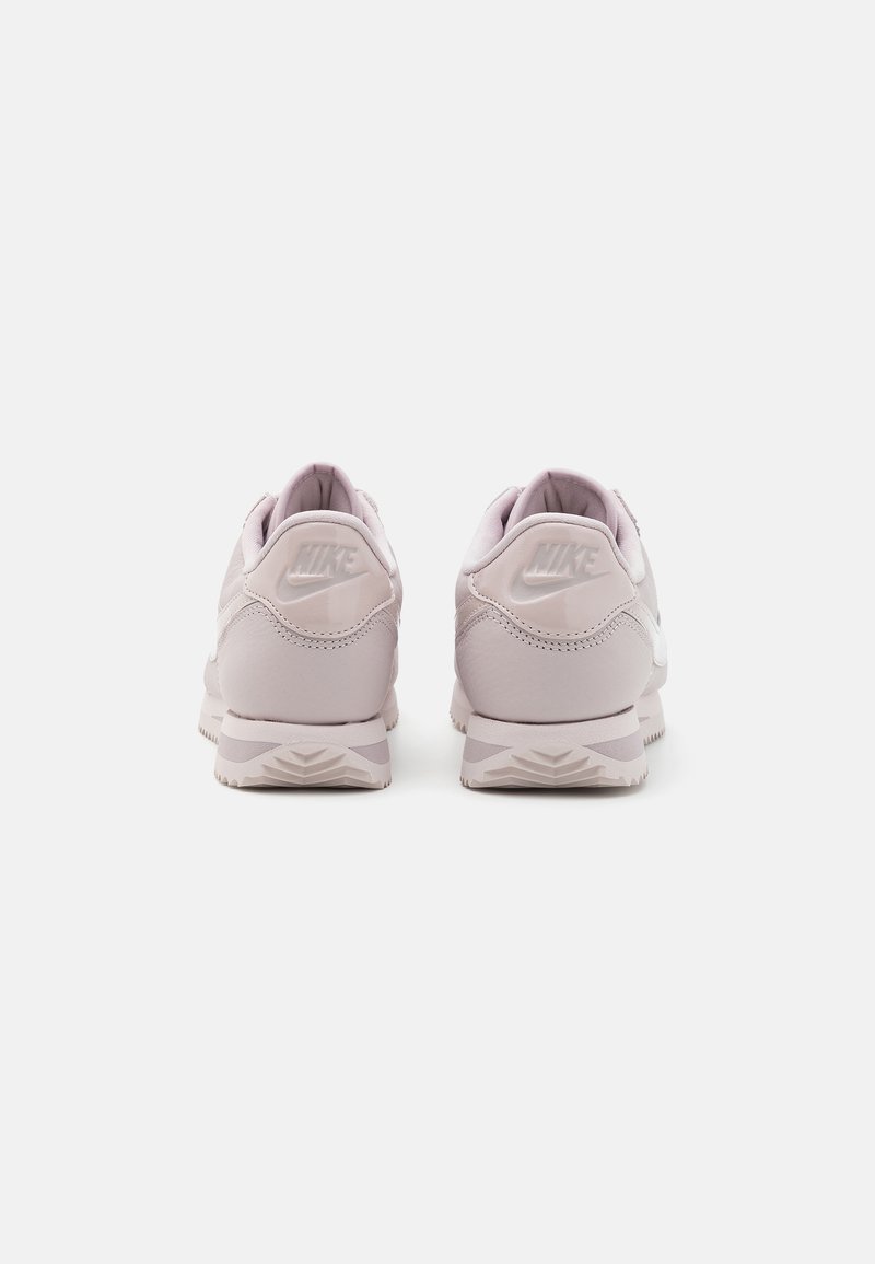 Zapatillas Nike de color púrpura claro con una parte superior suave, collar acolchado y suela texturizada, que presentan un sutil logotipo en relieve en el talón.