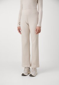 Ribbet, højhælte beige bukser med en flared ben-design. Kombineret med lyse sportsko. Glat tekstur og strikket materiale.