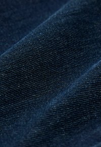 Tela de mezclilla azul oscuro, con una textura suave y un tejido de sarga visible. La superficie presenta ligeras variaciones en profundidad y brillo.