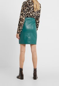 Jupe mini en cuir vert d'eau avec une coupe ajustée et une texture lisse, associée à un blouse à imprimé animal à manches longues et des bottines noires.