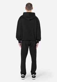 Black corduroy hoodie with a large hood, slightly oversized fit, ribbed texture, paired with black corduroy pants and white sneakers.