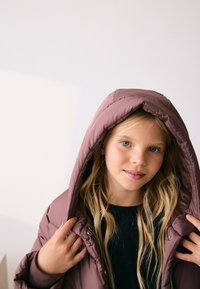 Fioletowa puchowa kurtka z kapturem, zapinana na zamek, z ściągaczami na rękawach. Miękka w dotyku, lekko wypełniona, o eleganckim fasonie.