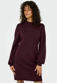 Abito a maglia bordeaux con maniche lunghe e puff, collo alto e silhouette aderente, caratterizzato da polsini e orlo a costine. Tasche non visibili.