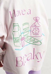 Roze oversize dukserica sa zabavnim grafikonima pakiranja mlijeka, staklenke džema i štruce kruha, uz natpis "Uzmi pauzu".